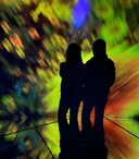 Two people stand in silhouette in front of a vivid, abstract light display with swirling green, yellow, blue, and red tones.