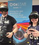 Two workshop participants wearing mixed reality headsets hold VR controllers while taking part in an interactive demonstration in front of CoSTAR Screen Lab branding.