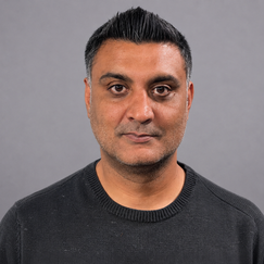 A man looking at the camera from chest up with brown skin and dark hair smiling