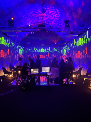 A group of people in a room with lights around computers with silhouettes of people with a person in a wheelchair