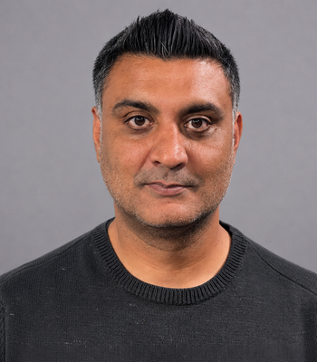A man looking at the camera from chest up with brown skin and dark hair smiling