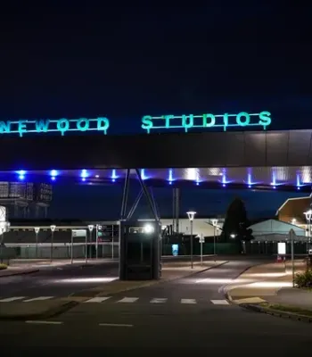 Nighttime exterior view of Pinewood Studios entrance with a blue neon sign, modern canopy, and illuminated walkway.
