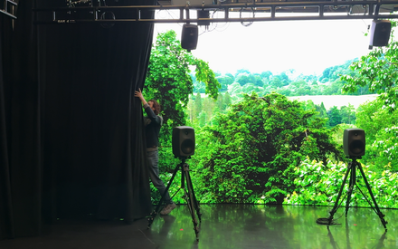 A person drawing back a curtain to reveal a large virtual production LED screen inside the spatial audio studio at CoSTAR National Lab, Futures Studio, Egham