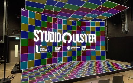The CoSTAR Screen Lab LED stage showing a colourful background of different coloured squares. There is a logo lock-up overlay including the logos of Studio Ulster and Ulster University.