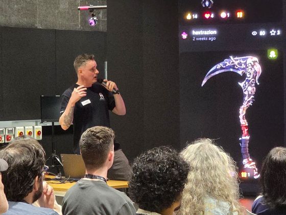 A speaker holding a microphone presents to an audience beside a large screen showing digital artwork and social media-style interface graphics during the AI for Creativity workshop.