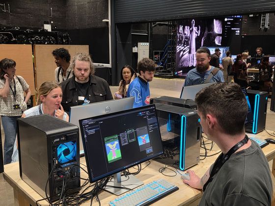 Workshop attendees stand around computer stations displaying node-based creative software while networking and participating in demonstrations inside Studio Ulster’s production space.