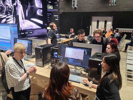 Workshop attendees gather around computer workstations displaying animation and AI software while discussing creative workflows inside the virtual production stage at Studio Ulster.