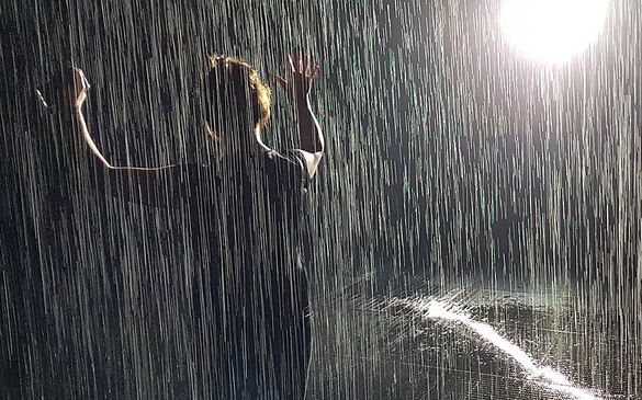 Photo of person holding hands up as if dancing in the rain with what looks like rain and a bright spotlight behind them
