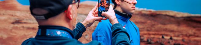 a man holding a phone up and taking an image of another man standing in front of virtual production screen