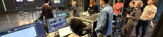 People in a studio surrounded by equipment with AI images on VP screen in background and actors learning scripts 
