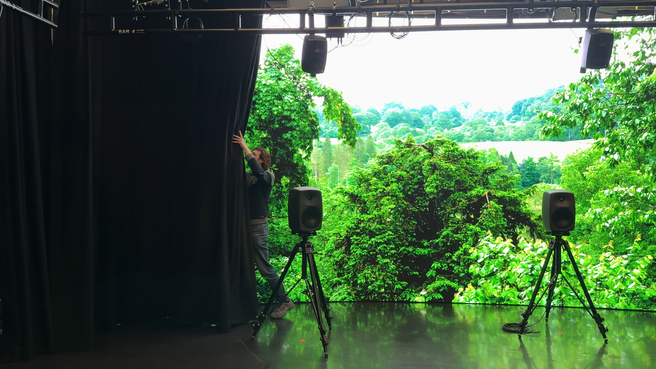 A person drawing back a curtain to reveal a large virtual production LED screen inside the spatial audio studio at CoSTAR National Lab, Futures Studio, Egham