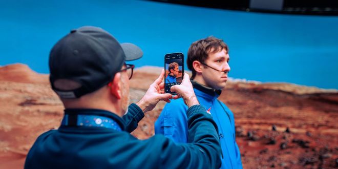 a man holding a phone up and taking an image of another man standing in front of virtual production screen
