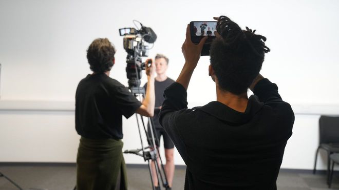 two men photographing and filming a stunt actor in a studio