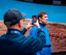 a man holding a phone up and taking an image of another man standing in front of virtual production screen