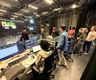 People in a studio surrounded by equipment with AI images on VP screen in background and actors learning scripts 