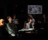 a group of people sitting at tables in a darkened room focusing on something to the right of screen two men and two women are in view