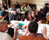 a group of about 20 diverse people in a room sat round tables taking part in a workshop with animated expressions